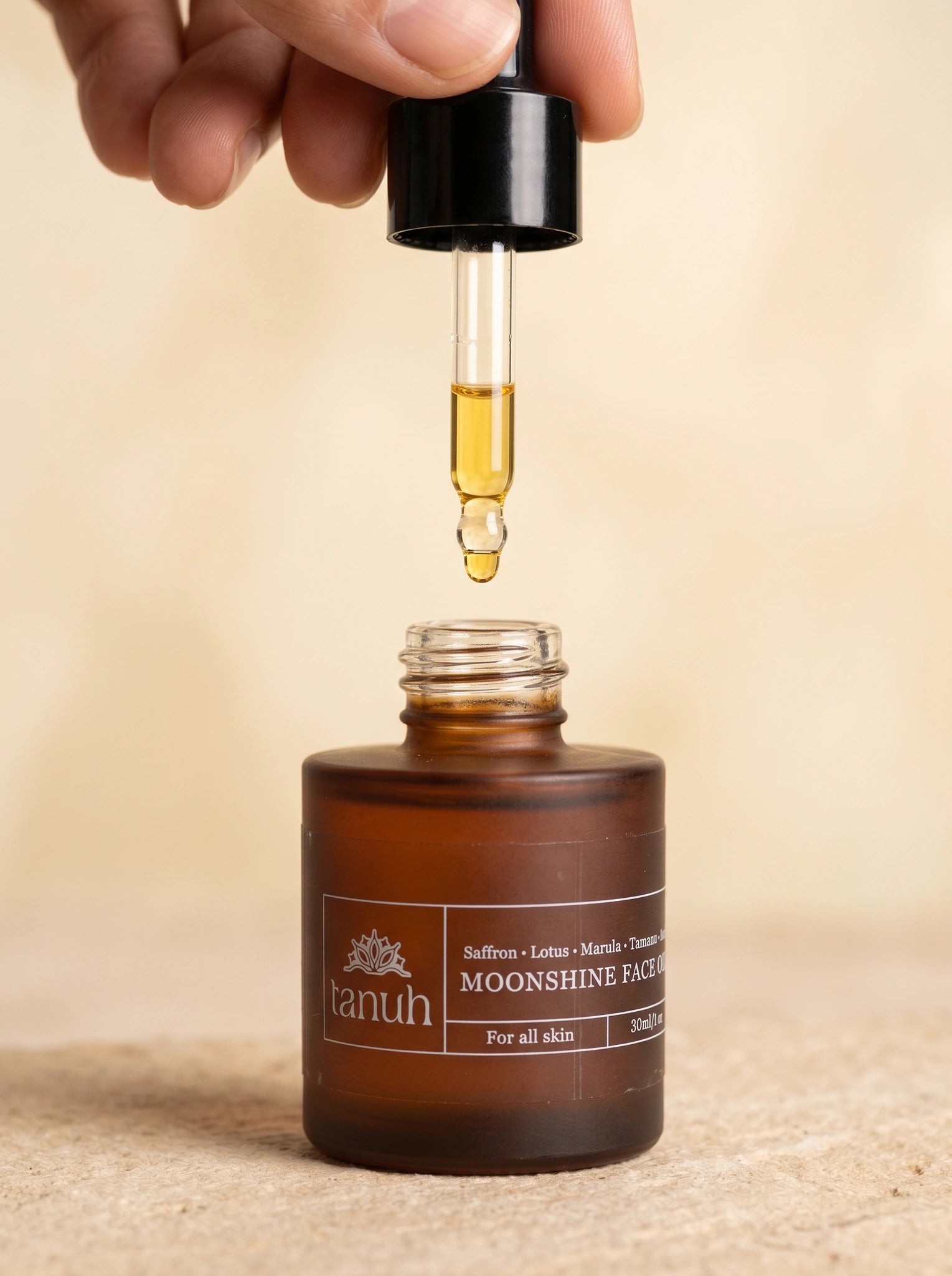 Dropper of golden Tanuh Moonshine face oil held above the open amber bottle, showing the saffron-infused oil