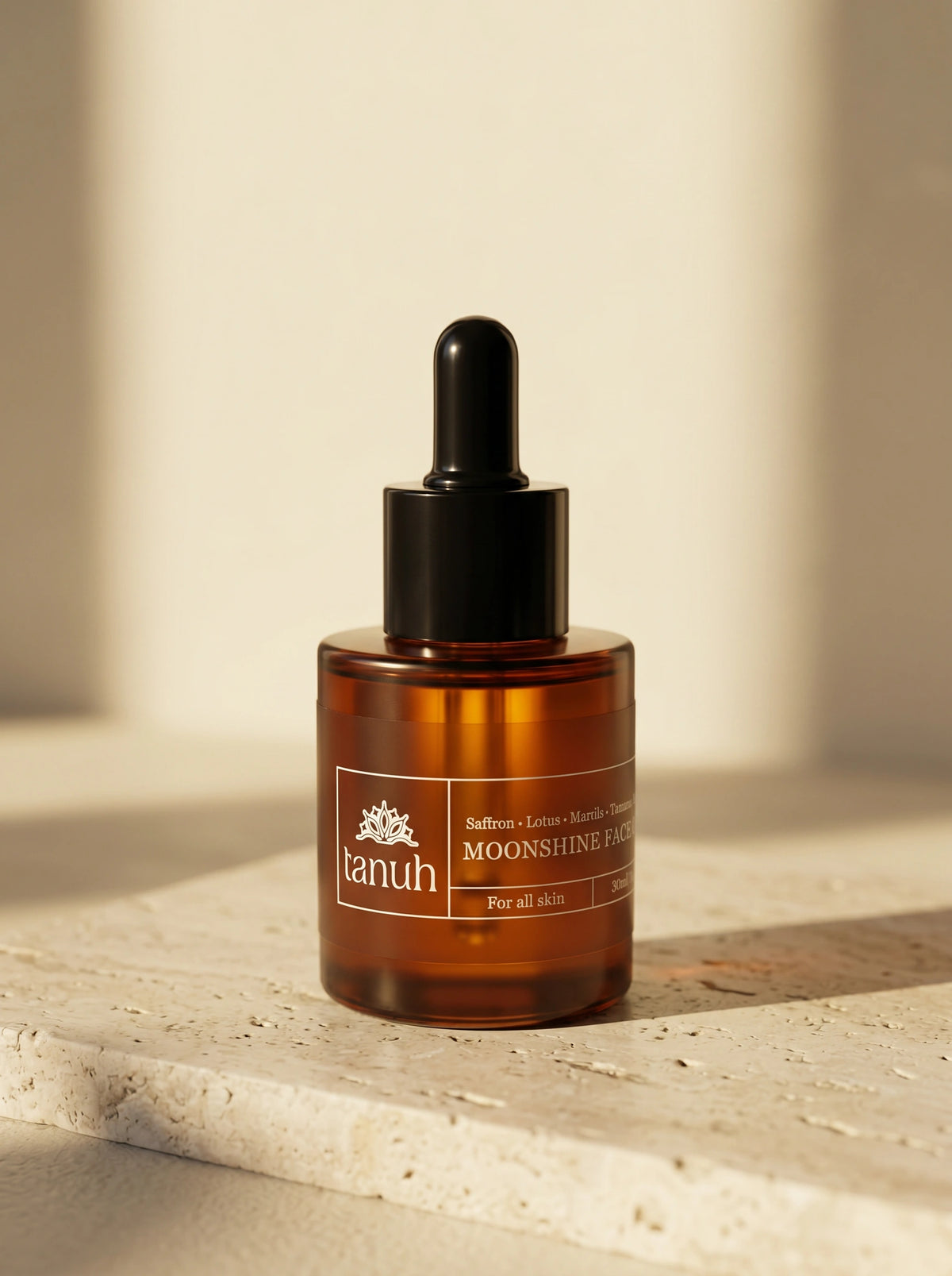 Tanuh Moonshine face oil — amber glass bottle with black dropper on travertine stone, saffron kumkumadi night oil, 30ml