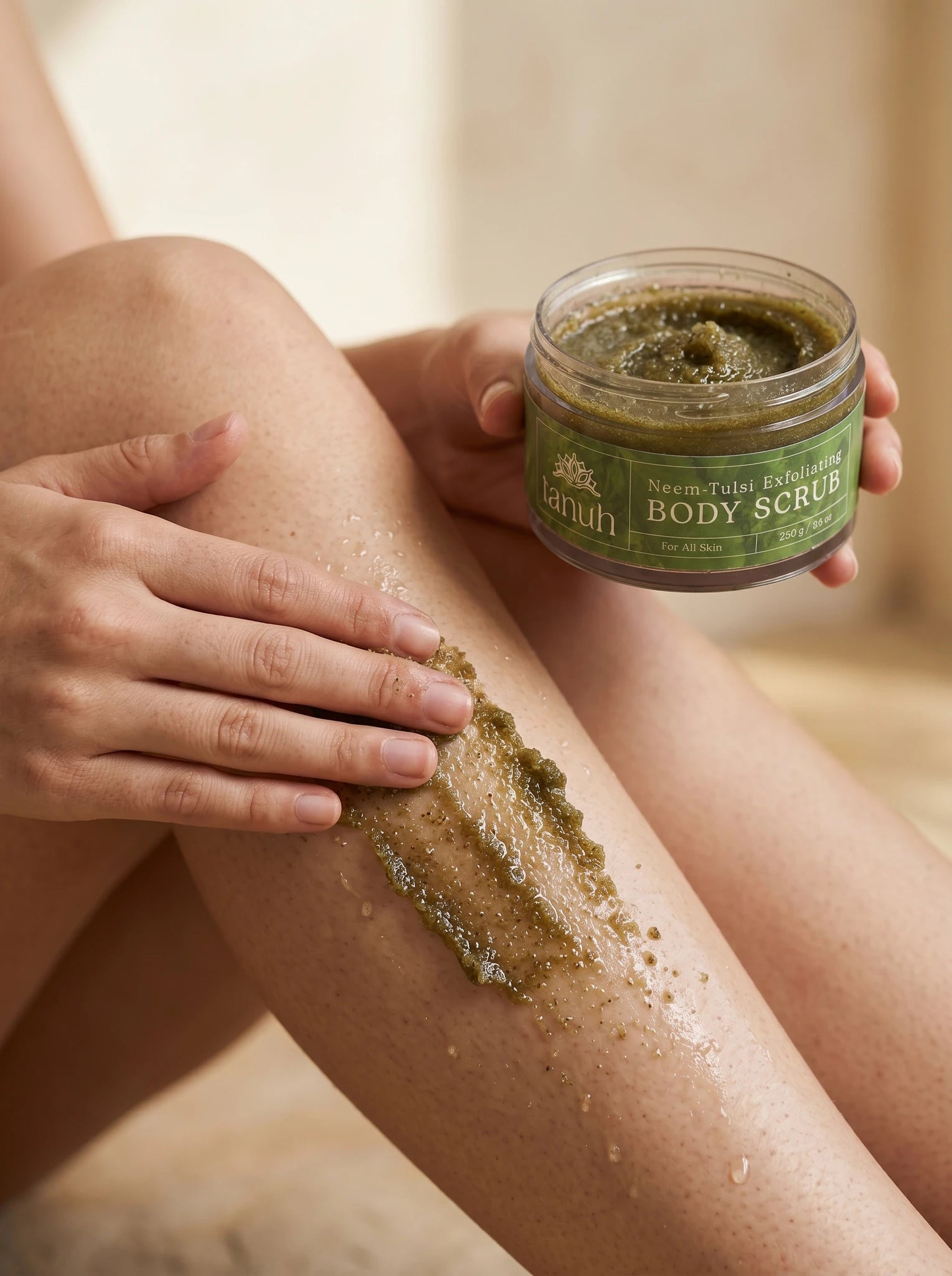 Applying Tanuh Neem & Tulsi body scrub to the leg — green exfoliating scrub spread on skin